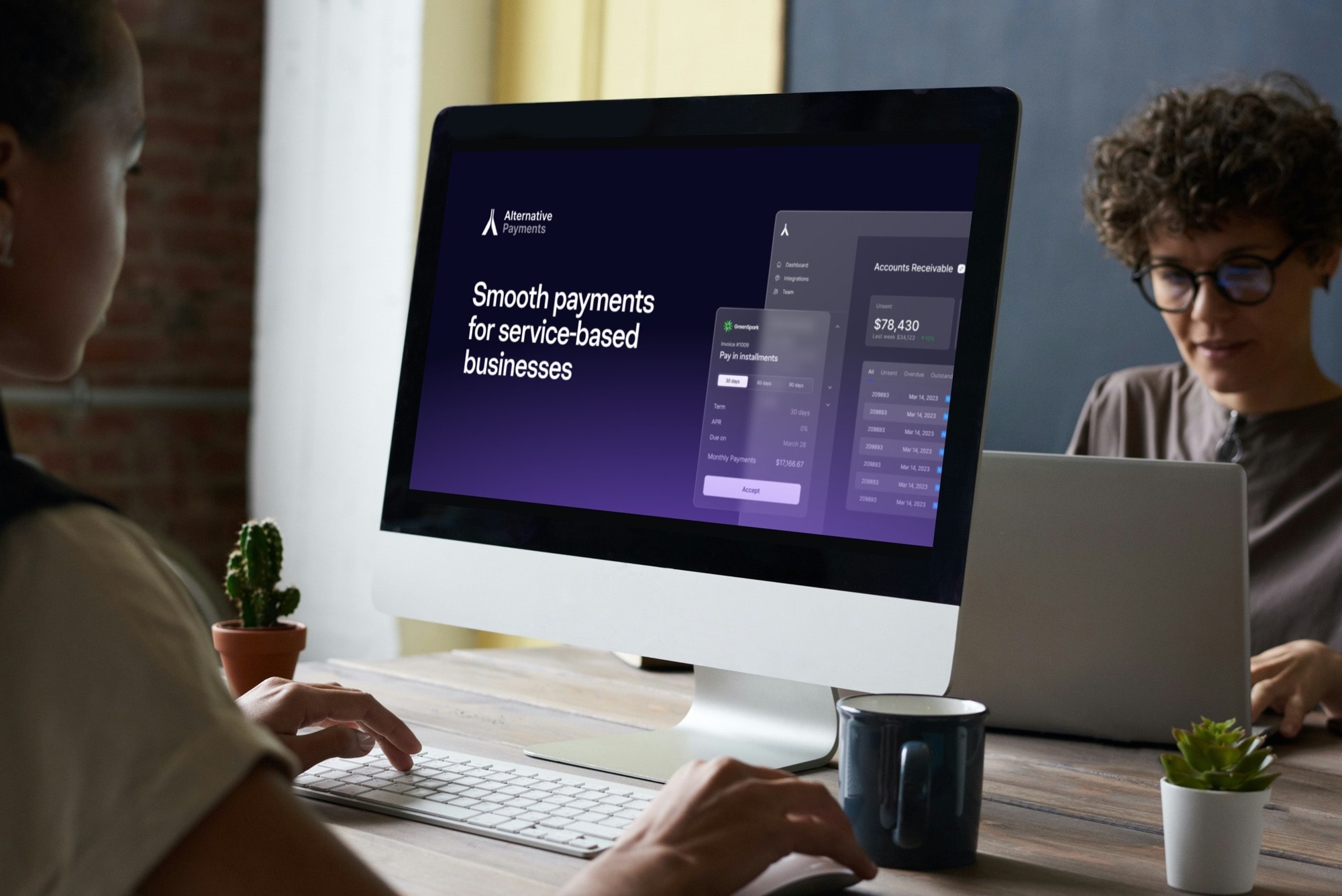 Accounts Receivable Management portrayed in an image of a office setting where there are people sitting in chairs on the outskirt of the photo and in the background. The foreground of the image is a desk with a notepad, pen cup holder, keyboard, mouse, and desktop apple computer. On the computer screen is the homepage for the Alternative Payments website where you can understand how best to choosing the right Payment Service Provider. The website in the image has the wording "Smooth payments for service-based businesses" set on a dark blue, navy, and purple color scheme. Above the computer is a window with light beaming through from the sun outside.